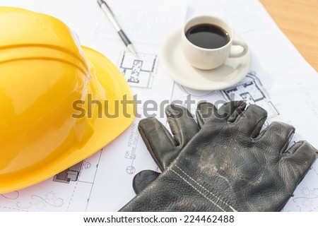 Close up work black glove with coffee, safety helmet and floor plan drawings on the table