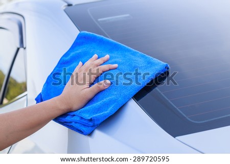 Close up woman hand with blue microfiber cloth cleaning the car