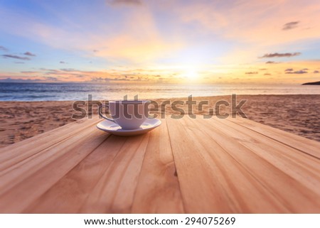 Close up coffee cup on wood table at sunset or sunrise beach