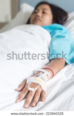 Female patient with IV drip needle piercing on hand in hospital room, Focus on hand