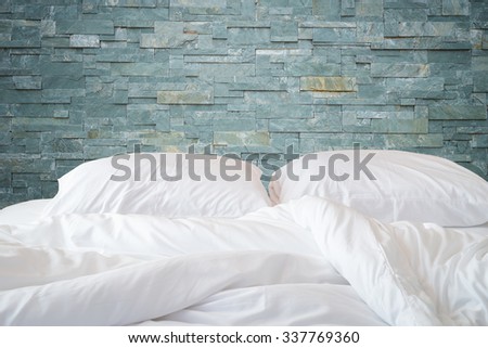 Close up white bedding sheets and pillow on natural stone wall room background, Messy bed concept
