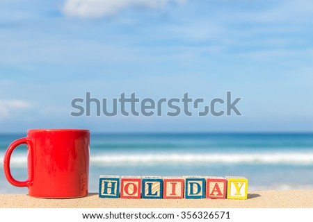 word HOLIDAY in colorful alphabet blocks and coffee cup on tropical beach, Phuket Thailand