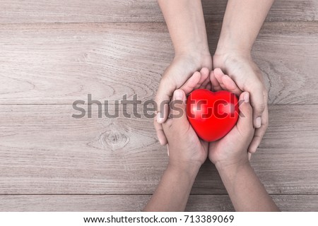 Love Mom Concept : Woman holds her young kids hands supporting red heart on brown wooden table background. Free space for text of Mother\'s Day celebration.