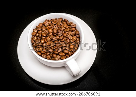 Coffee beans in a cappuccino cup on a black granite surface