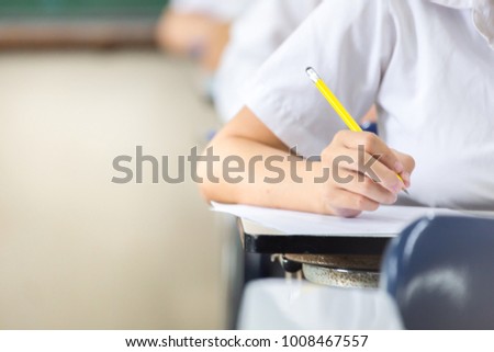 soft focus.high school or university student holding pencil writing on paper answer sheet.sitting on lecture chair taking final exam attending in examination room or classroom.student in uniform