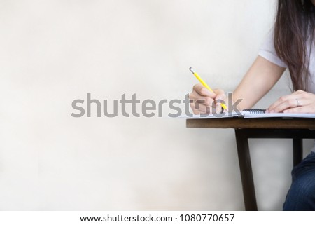 hand high school or university student in casual holding pencil writing on paper answer sheet.sitting on lecture chair taking final exam attending in examination room or classroom.