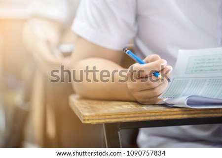 soft focus.hand high school or university student in uniform holding pencil writing on paper answer sheet.sitting on lecture chair taking final exam or study attending in examination room or classroom