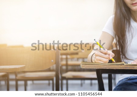 hand high school or university student in casual holding pencil writing on paper answer sheet.sitting on lecture chair taking final exam or study attending in examination room or classroom