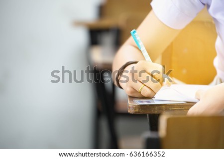 closeup hands university student holding pen writing doing examination with blurred background.students in uniform attending exam classroom educational school.space for text.