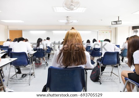 soft focus. back view abstract background of examination room with undergraduate students inside. university student in uniform sitting on lecture chair doing final exam or study in classroom.