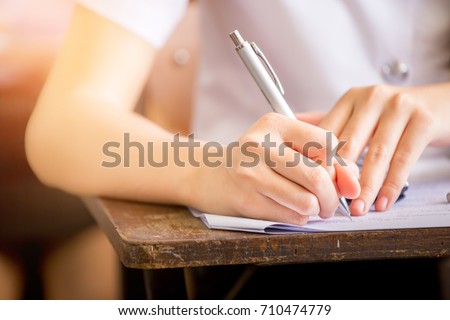 soft focus.high school or university student holding pencil writing on paper answer sheet.sitting on lecture chair taking final exam attending in examination room or classroom.student in uniform.