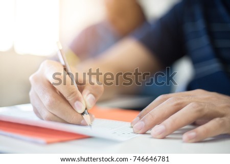 soft focus.high school or university student holding pencil writing on paper answer sheet.sitting on lecture chair taking final exam attending in examination room or classroom.