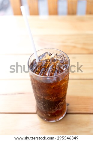 Glass of cola with ice on wooden table for drink when waiting for the food order.