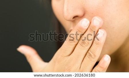 Extreme close-up of a young woman covering her mouth with her hand and looking shocked