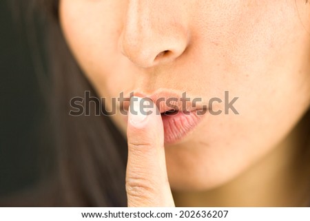 Extreme close-up of a young woman with finger on lips asking for silence