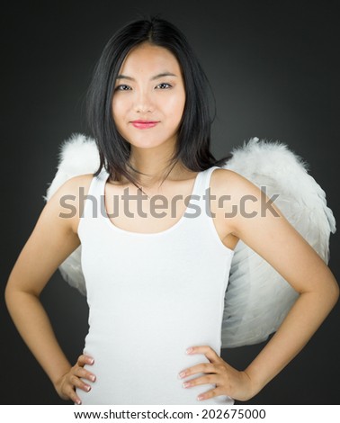 Confident Asian young woman dressed up as an angel with her arms akimbo