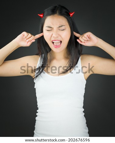 Asian young woman in devil horns and shouting in frustration with fingers in ears
