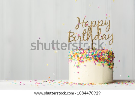 Colorful birthday cake with golden happy birthday banner and falling sprinkles