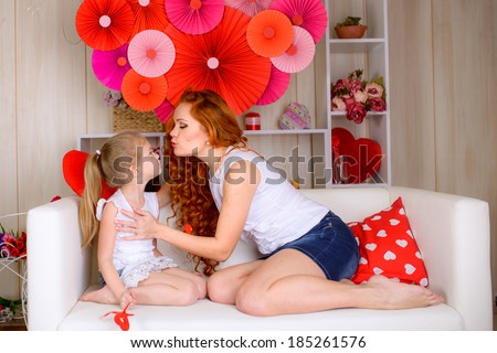 portrait of young mother kissing lovely daughter indoors