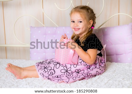 Portrait of attractive cheerful girl in pink dress holding gift box with pink bow on the bed