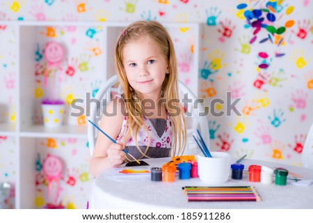 Cute little girl drawing with paint and paintbrush at home