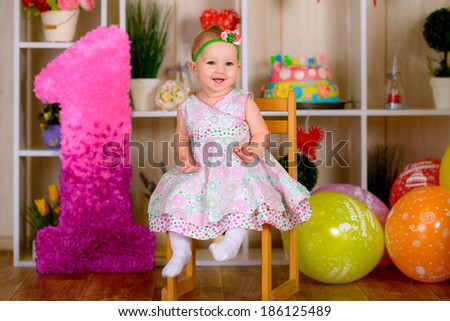 Cute funny little kid in first birthday with colored balloons in the bright room on the chair
