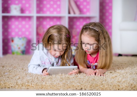 Kids together on the floor using tablet PC in the bright pink living room after school have a fun game
