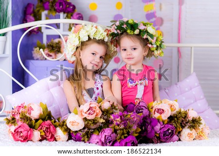 two Adorable smiling little girl friends with flowers on bed smiling