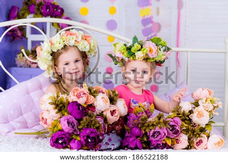 Adorable smiling little girl with flowers on bed with her friend smiling
