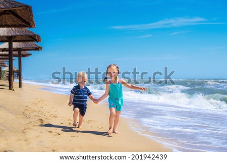 happy kids playing in a summer sea, running together along the beach ocean, fun game for boy and girl