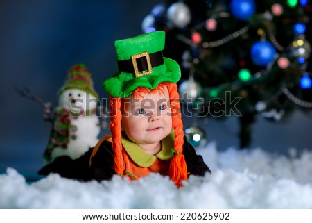 girl with lying on the carpet snow. Christmas tree in the background. smiles elf costume