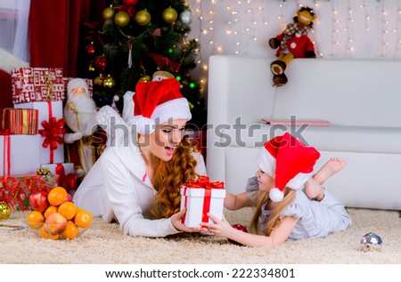 beautiful family mother and her baby on the floor near the Christmas tree on Christmas Eve give gifts to each other