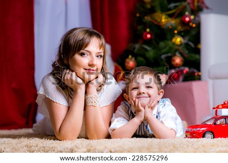Happy family on the floor in the Christmas evening with gifts at the Christmas tree with Christmas lights. children\'s car,
