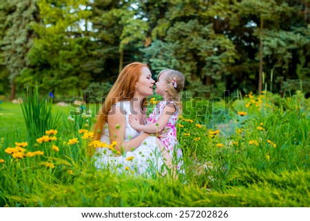 Mom and child in the park on the grass among flowers happily play together spring summer