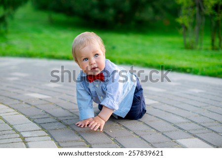 little baby in the park in jeans and a blue shirt in a red bow tie fun playing