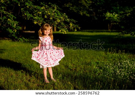 beautiful cute baby girl standing on the grass in the forest clings to dress
