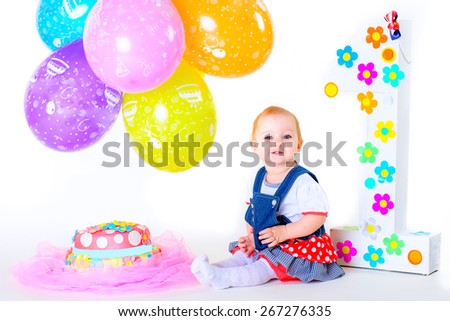 a small child sitting on a white background isolated in his birthday among balloons near the cake
