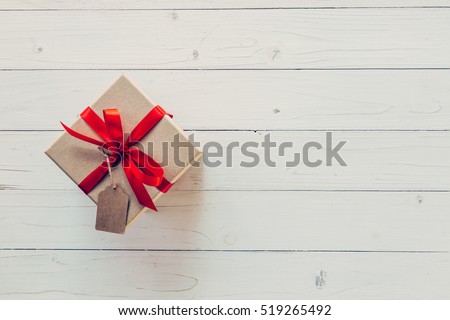 Brown gift box with tag on wooden background. Gift box with red ribbon on wood background with space.
