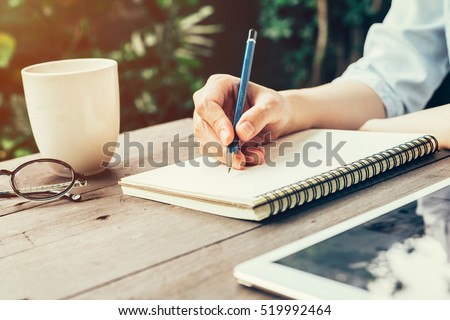 Woman hand with pencil writing on notebook at coffee shop. Woman working in outdoor at coffee shop.