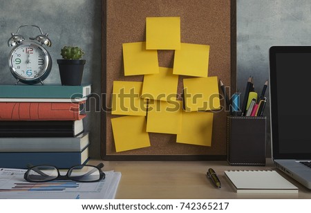 Resolutions, notes, goals, post, memo or action plan concept. Sticky notes on cork board in workplace office with laptop, notebook, eye glasses, clock, plant, books and stationery on wooden desk.