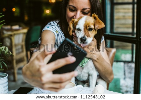 Young beautiful woman having great time with her little sweet dog in a restaurant after their meal, taking many pictures. Lifestyle and friendship concept.