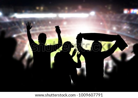 Friends at football game in soccer stadium. Crowd cheering and celebrating a goal in arena during match. Silhouette people in live sport audience having fun.