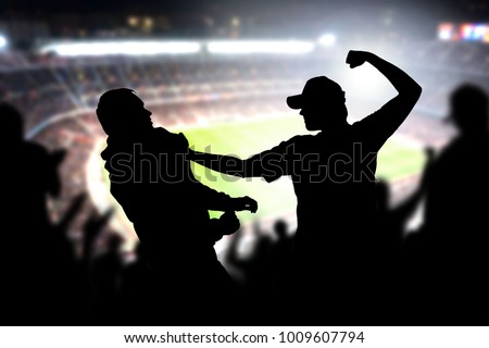 Fight in a football game crowd. Angry man hitting another spectator in soccer match audience. Violent argument between two fans of different teams and clubs. Hooligans and violence in sport event.