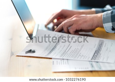Young man writing college or university application form with laptop. Student applying to school. Scholarship document, admission paper or letter on table. Typing email. Education and communication.