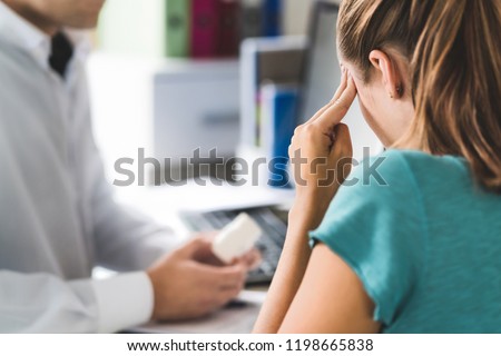 Doctor giving medical help to sick patient with bad headache or migraine. Physician or pharmacist holding bottle of pills and medicine in appointment. Woman suffering. Pain killers or antidepressants.