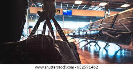 Terrorist in airport planning a bomb attack. Terrorism and security threat concept. Suspicious dangerous man in the shadows with black bag. Gate, bench and waiting area in the blurred background.