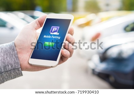 Mobile parking app on smartphone screen. Man holding smart phone with car park application in hand. Internet payment online with modern device. Row of vehicles in the background.