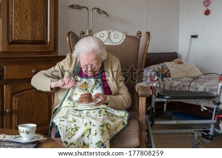 Old woman eats chocolate cake sitting on a chair in her room in an elderly home