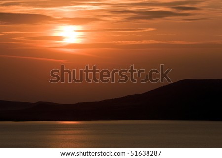 Morning on sea coast, red sun is reflected in water