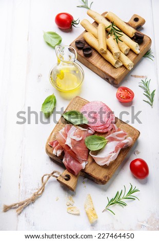 Grissini bread sticks, prosciutto ham, pancetta, salami, olive oil, basil on old wooden background